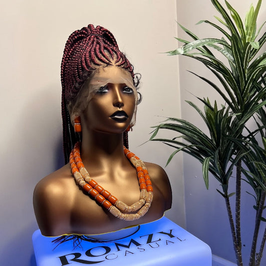 Full Lace braided wig with long red braids styled on a mannequin with dark skin tone, displayed with statement orange and gold necklace, next to a green plant.