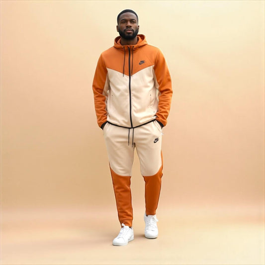 Man wearing white and orange Nike Tracksuit with hoodie and matching pants, standing against beige background